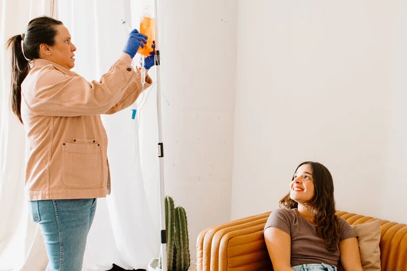 Mobile IV therapy in West Carson, CA by Lively Drops, a nurse hanging an IV bag while a client relaxes on a couch